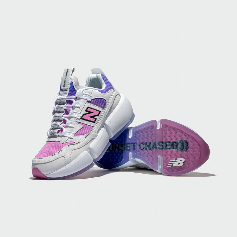 A pair of black NB Vision Racer sneakers with pink and purple accents against a light grey studio background