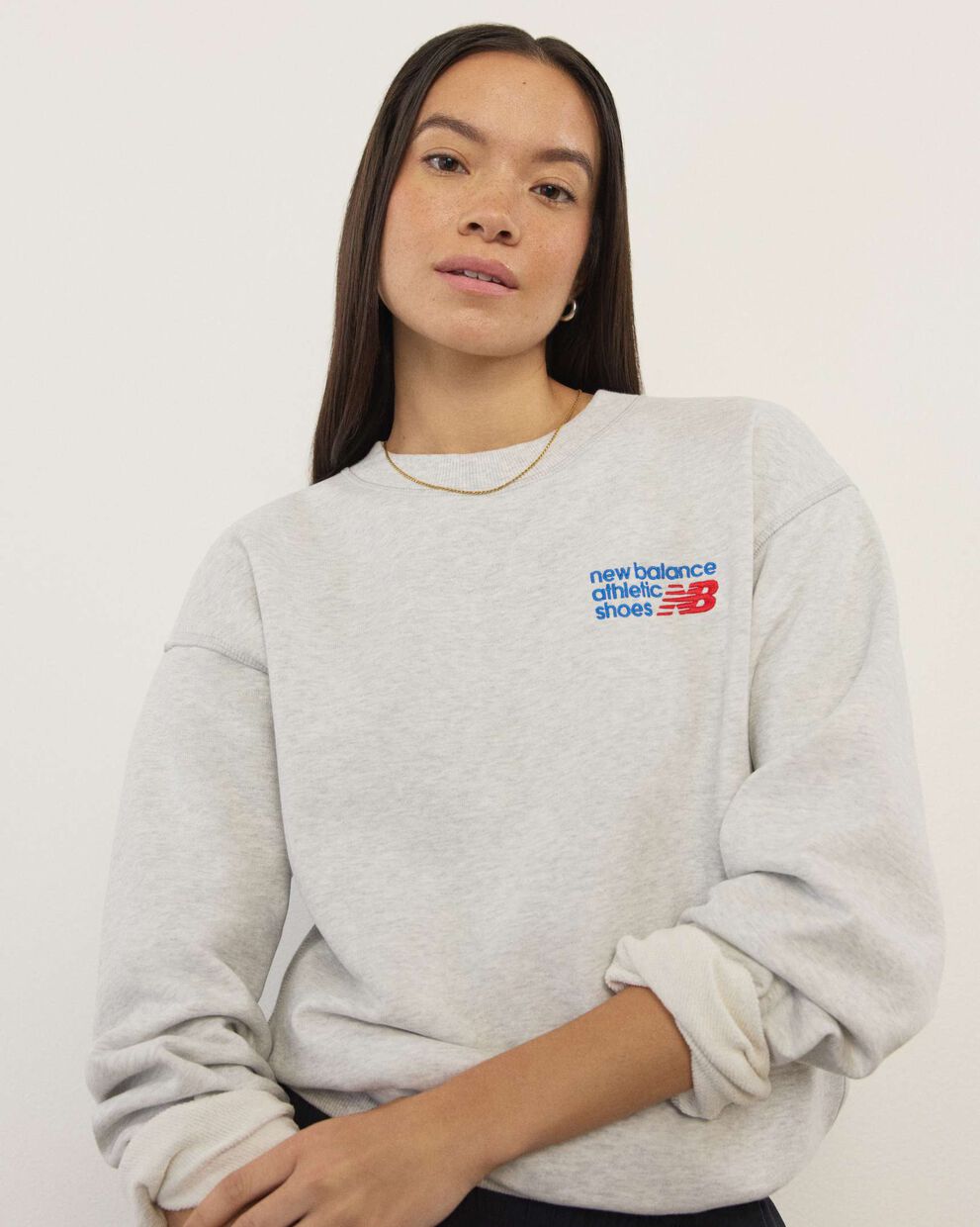 A woman wearing New Balance standing in front a white wall.