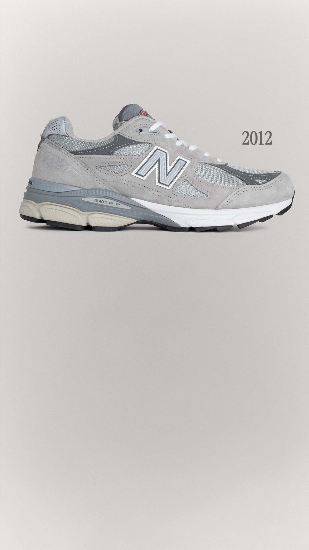 A grey 990v3 sneaker sitting on a grey background.