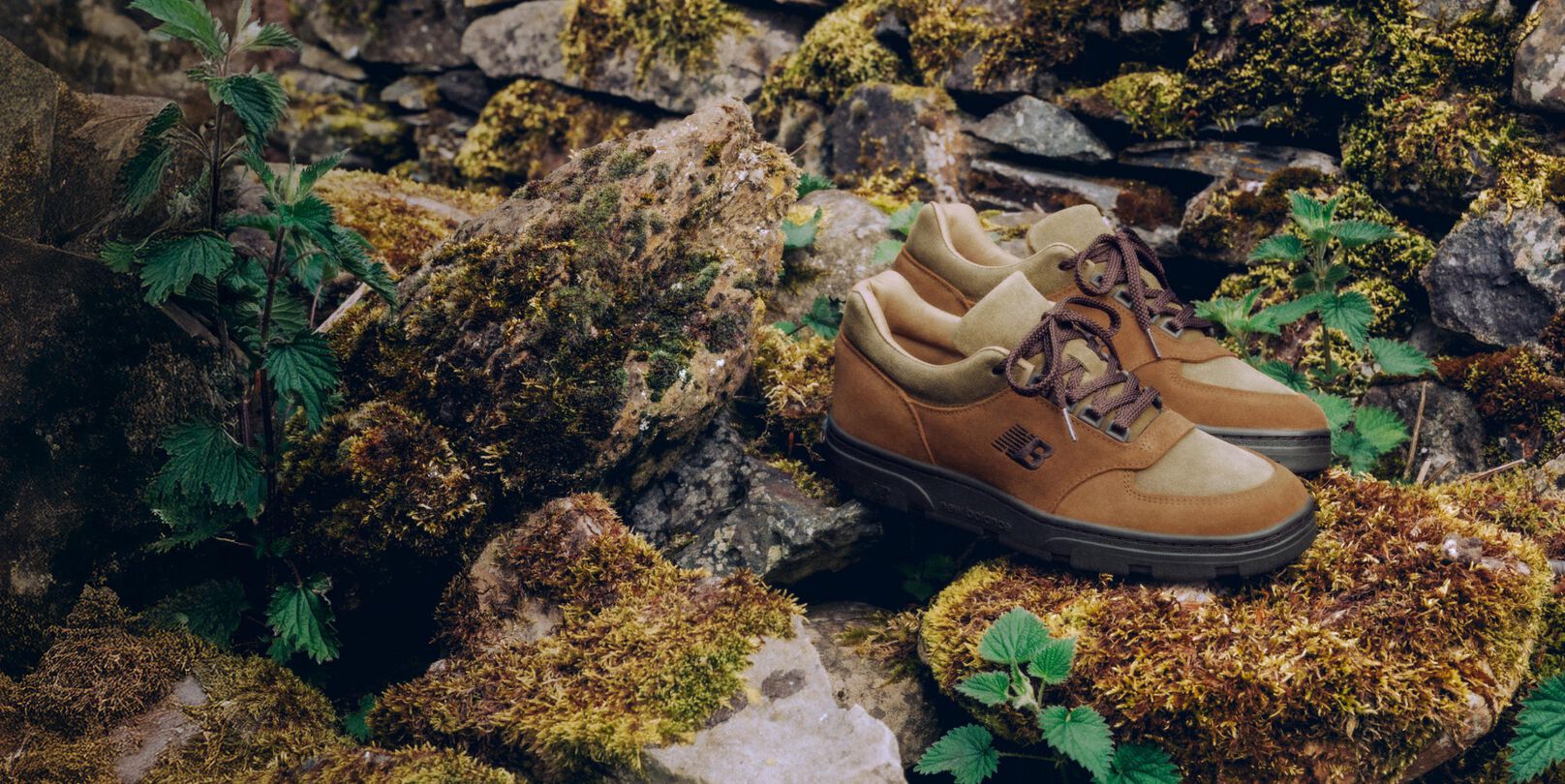 A pair of New Balance Made in UK sneakers sitting in a moss covered rock garden surrounded by small green plants. 