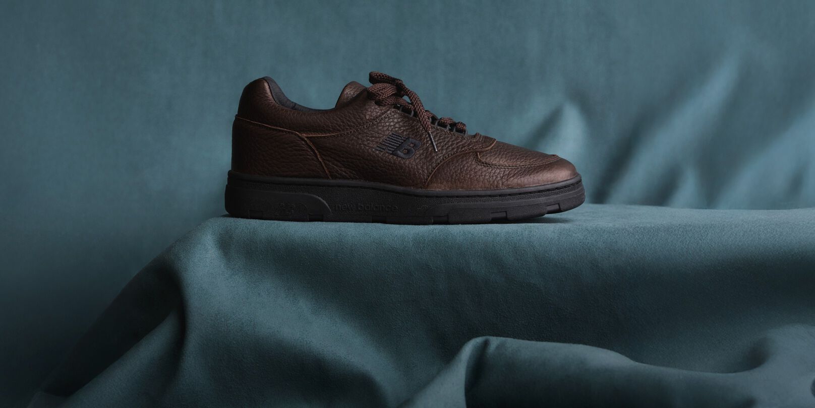 A New Balance Made in UK sneaker sitting in a flowing blue fabric studio backdrop. 