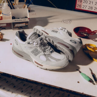A pair of New Balance Made in UK sneakers in front of a rabbit in a brown textured studio environment. 