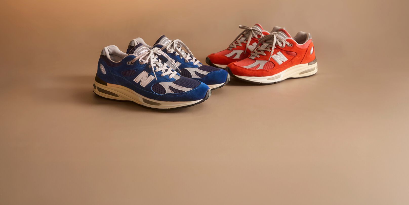 Two pairs of New Balance Made in UK sneakers in a beige studio environment. 