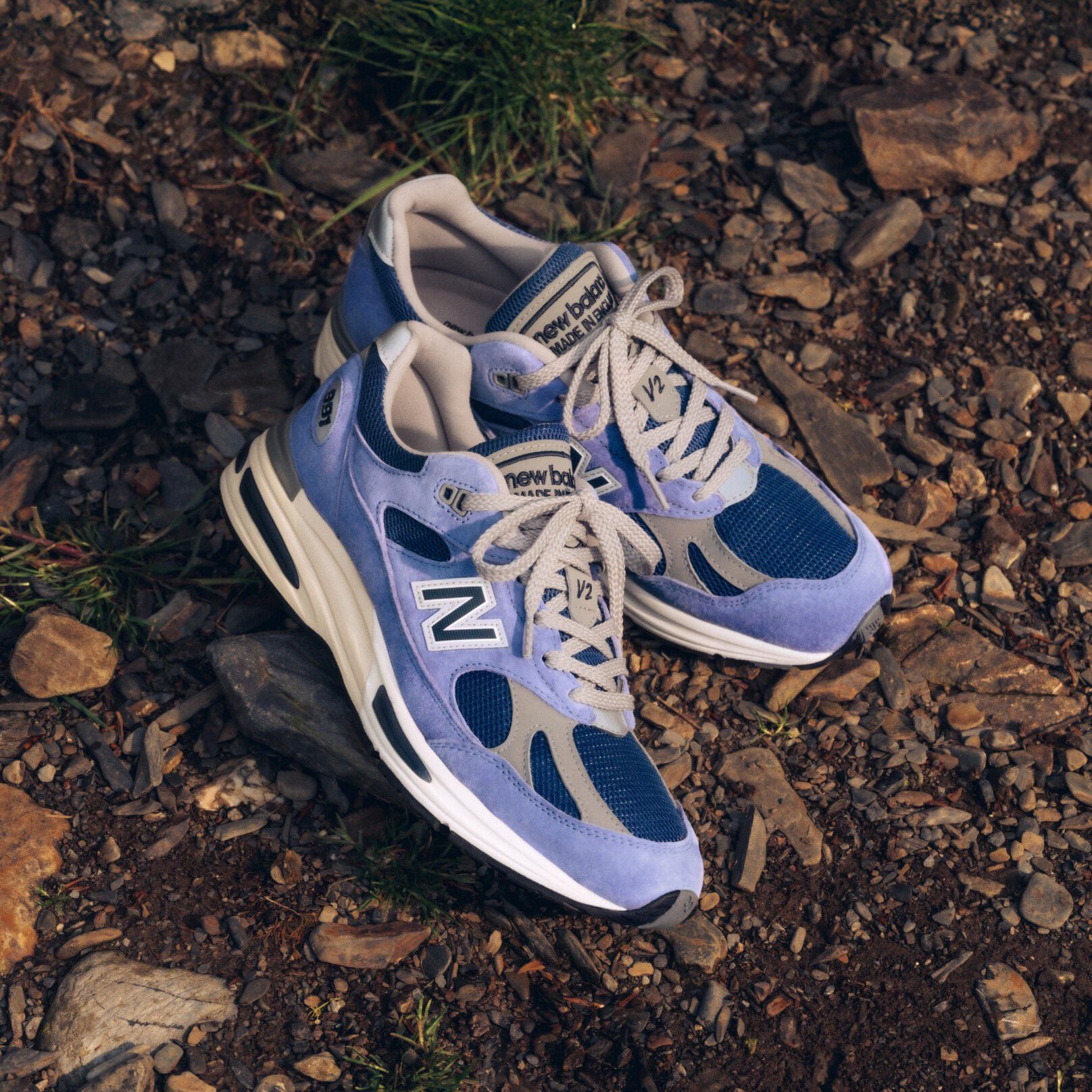 A pair of New Balance Made in UK sneakers on a raw earth surface of dirt and stones. 