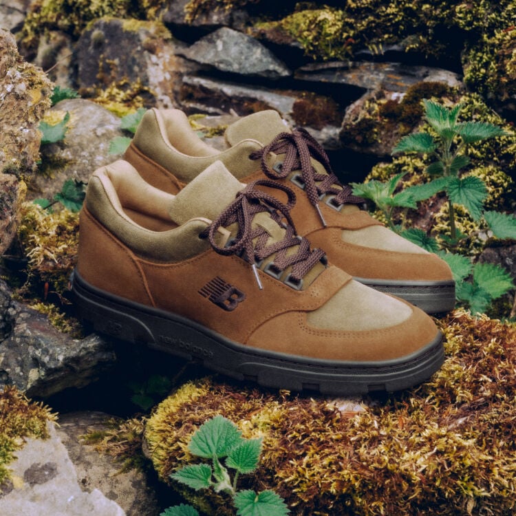 A pair of New Balance Made in UK sneakers sitting in a moss covered rock garden surrounded by small green plants. 
