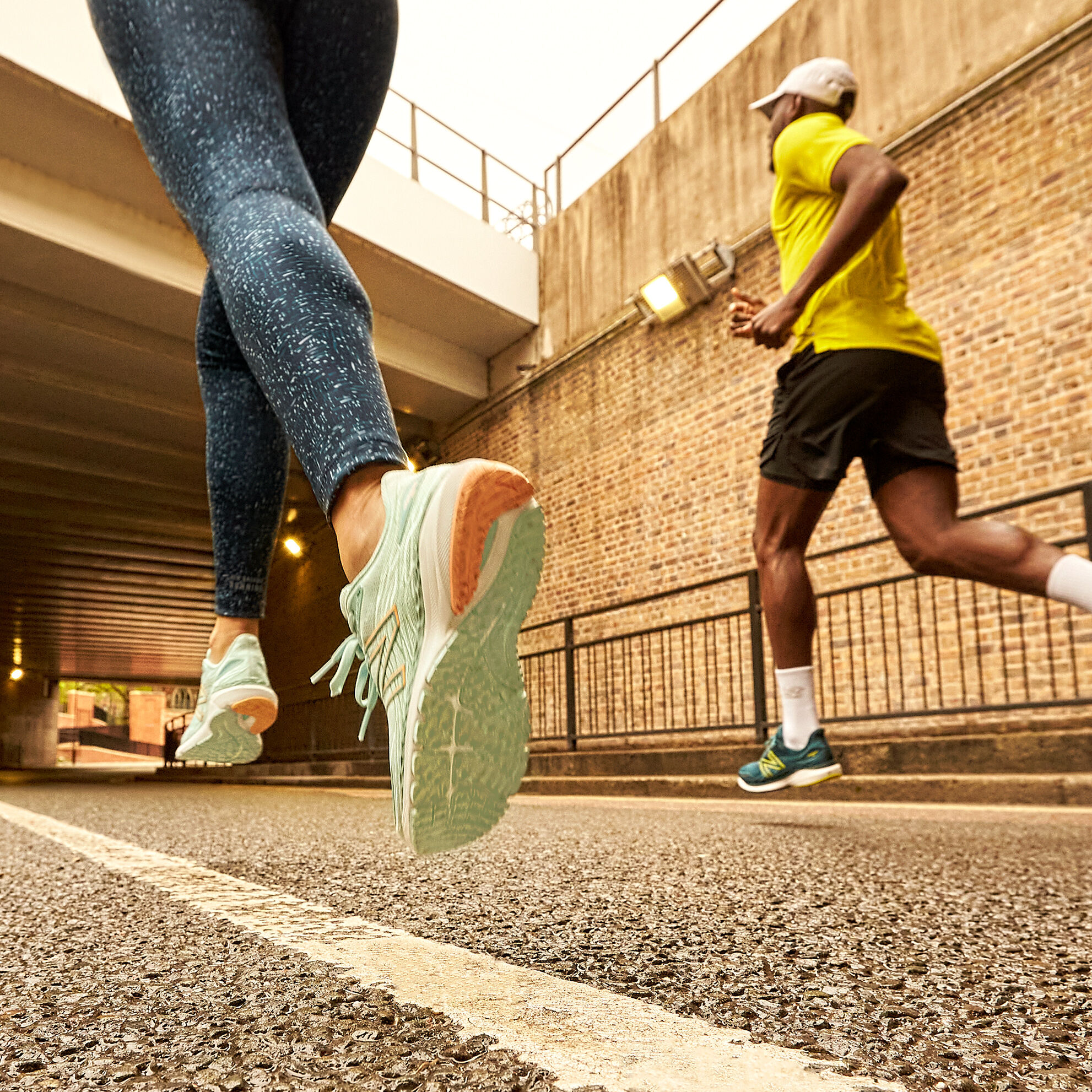Knee down crop of a female and male runner, female wearing patterned blue leggings and light blue Fresh Foam 860v12 and male wearing a yellow shirt, black shorts and dark green Fresh Foam 860v12