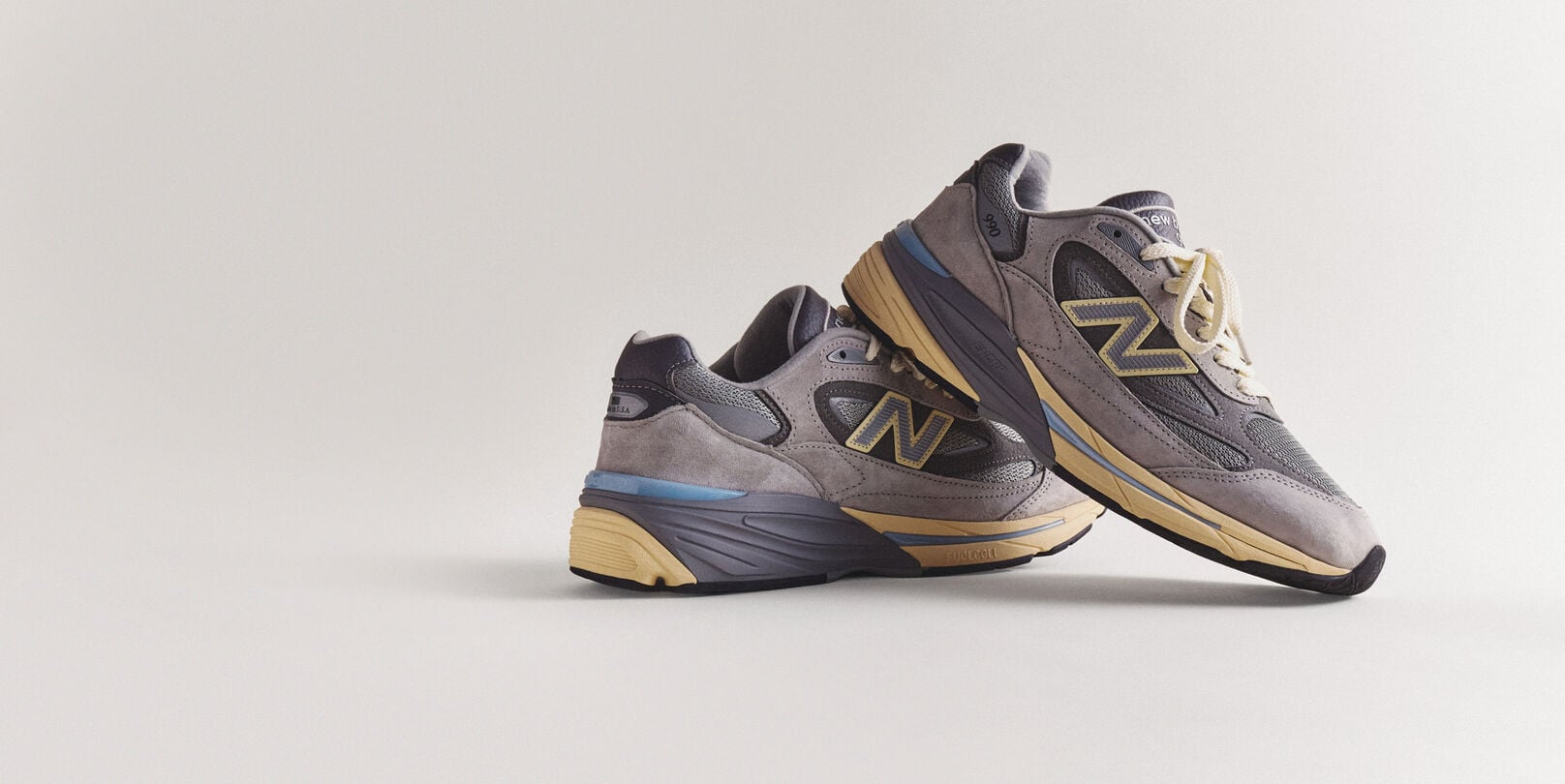 A pair of grey 990v7 sneakers sitting on a grey studio backdrop.