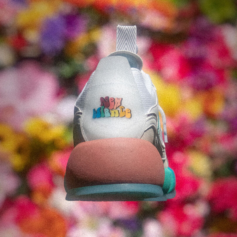 Back of a white Vision Racer floating that shows a modified New Balance logo with a blurred flower background behind it.