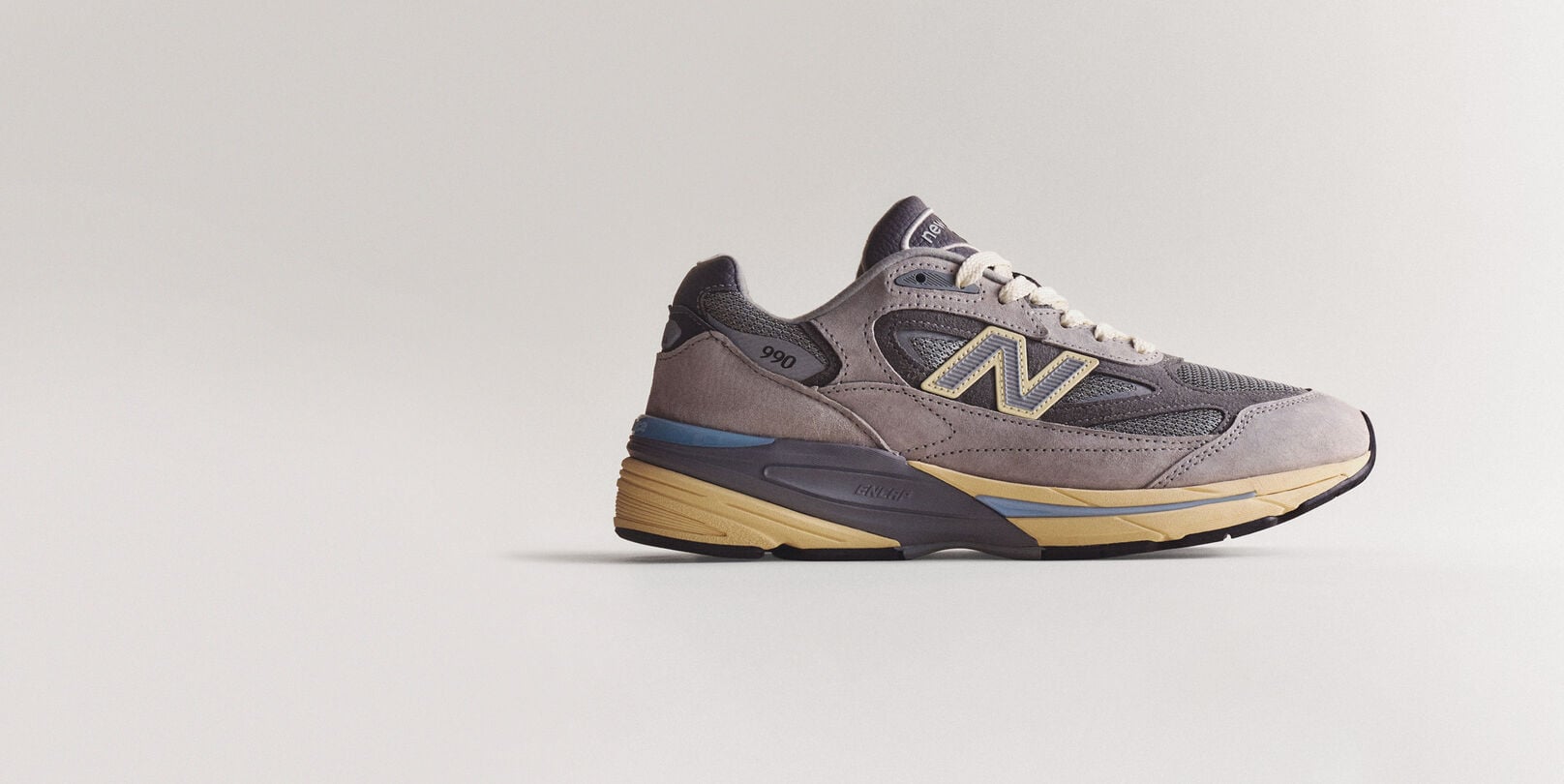 A grey 990v7 sneaker sitting on a grey studio backdrop.