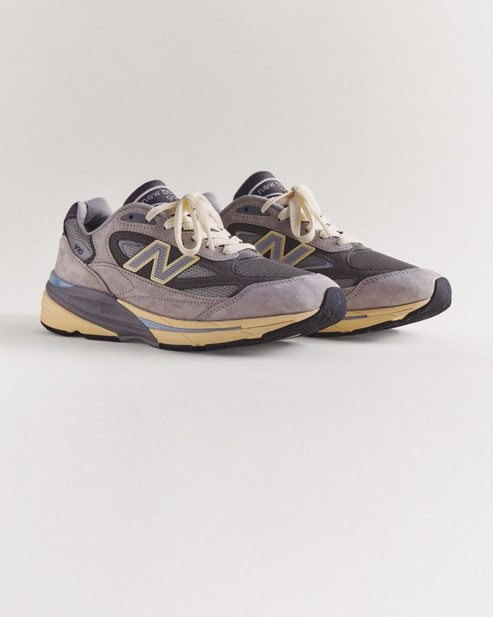A pair of grey 990v7 sneakers sitting on a grey studio backdrop.