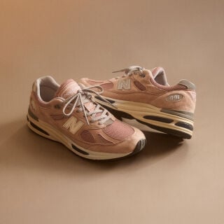 A pair of New Balance Made in UK sneakers in front of a rabbit in a brown textured studio environment. 