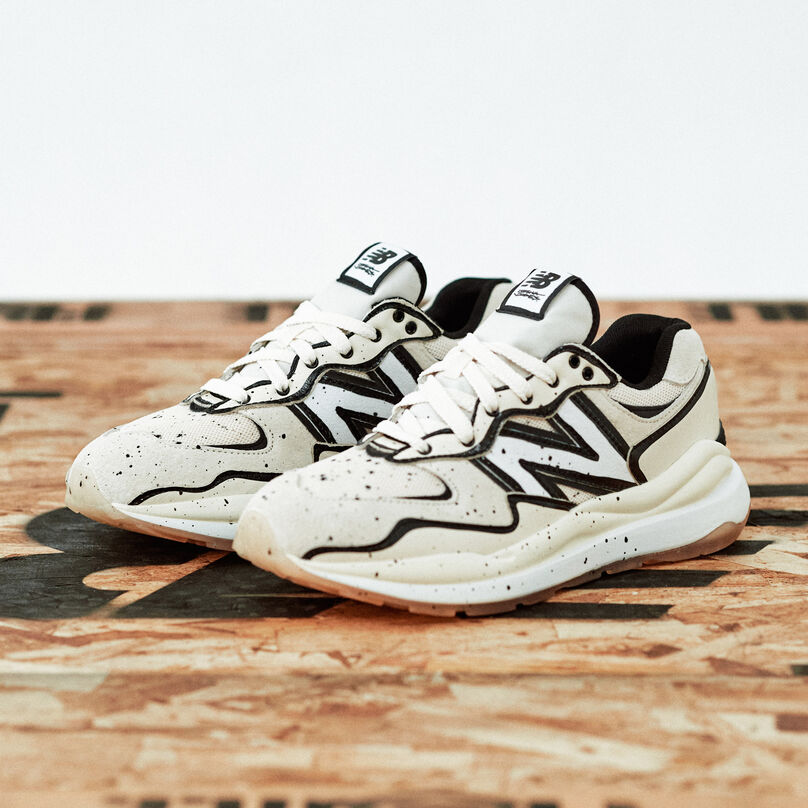White and black 57/40 sneakers sitting on a palette in a grey studio environment.